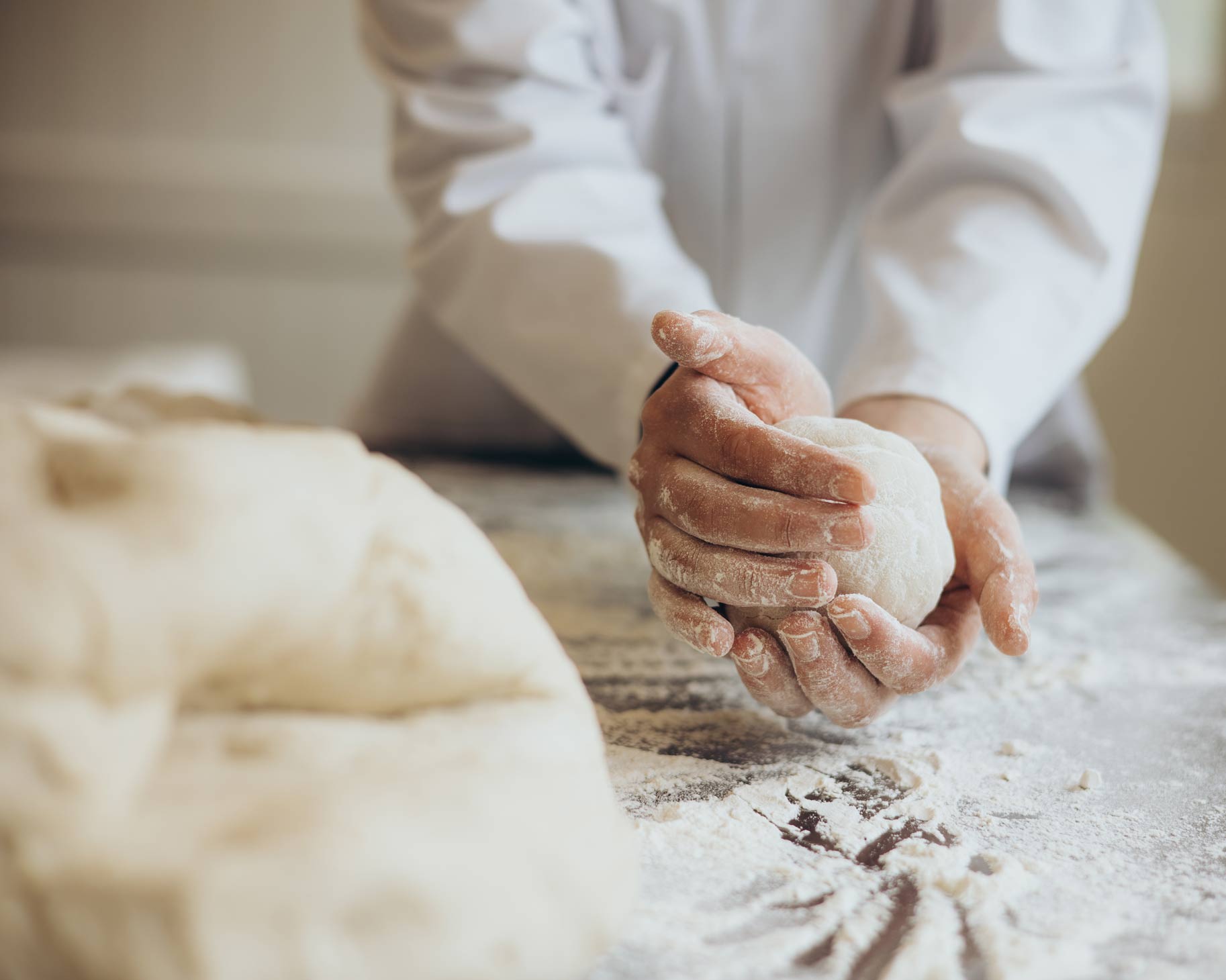 Hände formen eine Teigkugel auf bemehlter Arbeitsfläche